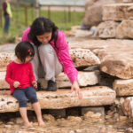 A woman and her daughter cooling off at the No Name Creek water feature at San Antonio Botanical Garden