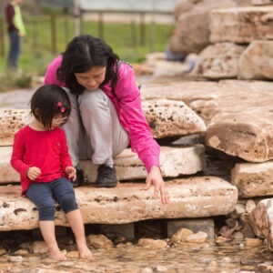 A woman and her daughter cooling off at the No Name Creek water feature at San Antonio Botanical Garden